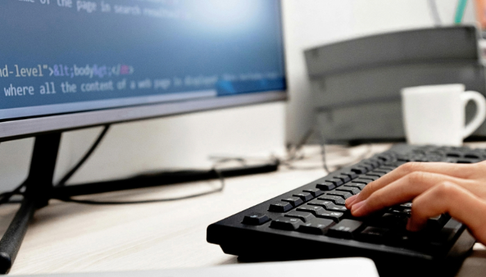 hands typing on a computer keyboard with code displayed on the screen