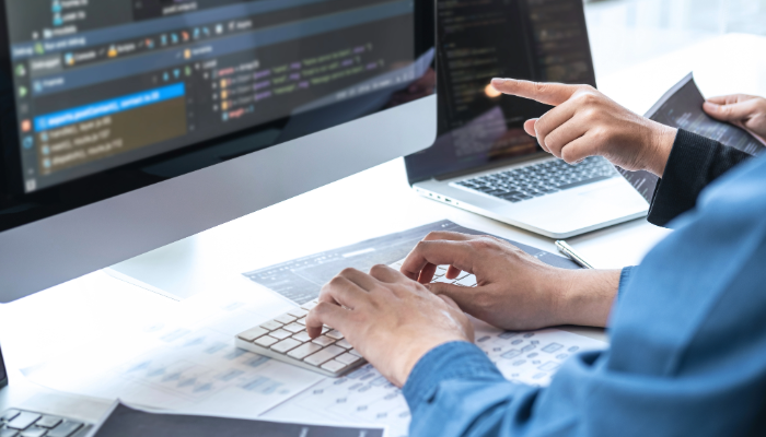 hands typing on a computer keyboard with code displayed on the screen